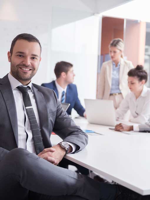Young bearded man in a grey business suit with a meeting with two women and one other man - all in business attire