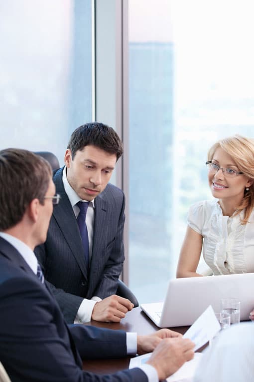 Two men in suits and a woman meeting and discussing a document in an office<br />
