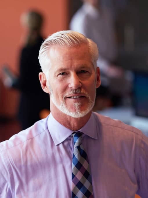 Mature man with a grey beard wearing a lilac short sleeved shirt and patterned tie